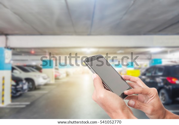 Man using touch screen mobile phone with blur\
cars parking