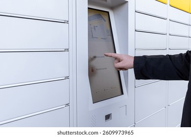 Man using touchscreen on white parcel locker terminal to collect or send package via modern contactless delivery system on urban street