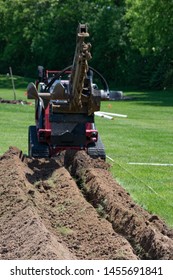 Man Using Trenching Equipment To Dig A Trench In A Green Yard To Lay PVC Pipe For Water Drainage