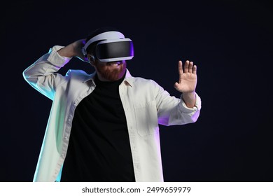 Man using virtual reality headset on dark background in neon lights. Space for text