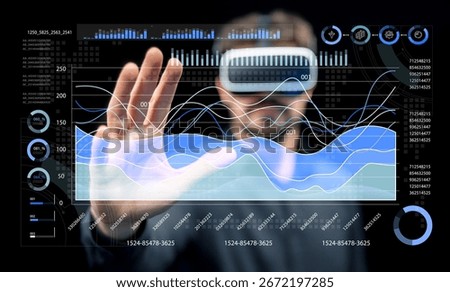 A man using a virtual reality headset interacts with an advanced digital interface displaying data visualizations, reflecting innovation in immersive technology and user engagement.