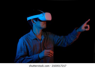 Man is using VR or virtual reality on black background. He is pointing. The new world of metaverse to connect people and the future for education and learning.  - Shutterstock ID 2103517217