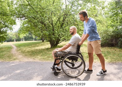 A man using a wheelchair sharing a joyful moment with his friend outdoors. They are in a leafy park, emphasizing friendship and inclusion.