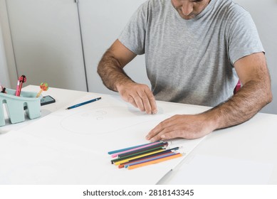 A man using a white rubber eraser to correct a pencil sketch on large paper surrounded by colored pencils.
