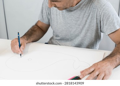 A man using a white rubber eraser to correct a pencil sketch on large paper surrounded by colored pencils.