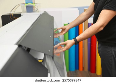 Man using wide-format printer indoors, closeup. Printing house