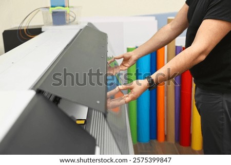 Man using wide-format printer indoors, closeup. Printing house