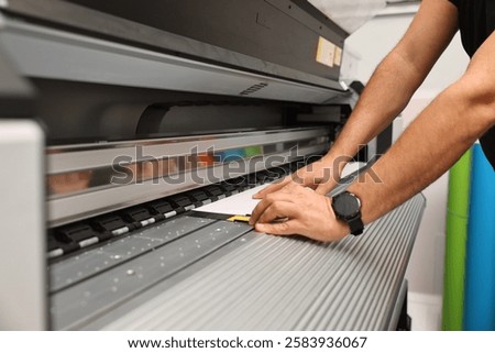 Man using wide-format printer indoors, closeup. Printing house
