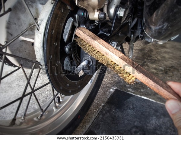 A Man is using wire brush to clean motorcycle\'s\
chain adjuster bolt.