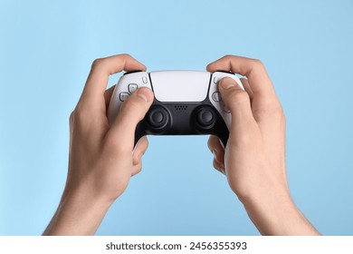 Man using wireless game controller on light blue background, closeup