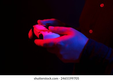 Man using wireless game controller on dark background in neon lights, closeup