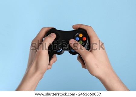 Man using wireless game controller on light blue background, closeup