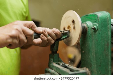 A man is using a woodworking machine to carve a piece of wood. The machine is green and has a wooden handle - Powered by Shutterstock