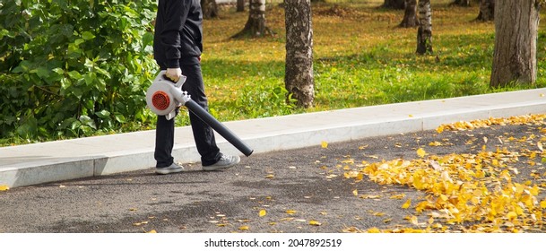 A Man, A Utility Worker, Removes Leaves From The Road With A Special Device.