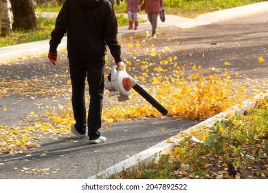 A Man, A Utility Worker, Removes Leaves From The Road With A Special Device.