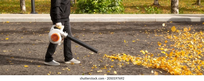 A Man, A Utility Worker, Removes Leaves From The Road With A Special Device.