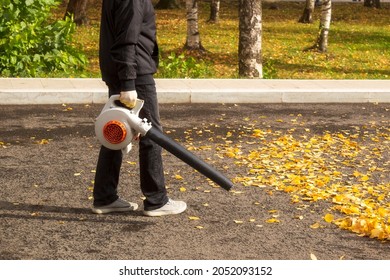 A Man, A Utility Worker, Removes Leaves From The Road With A Special Device.