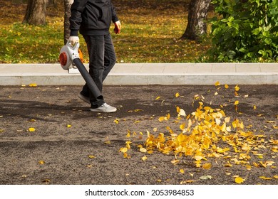 A Man, A Utility Worker, Removes Leaves From The Road With A Special Device.