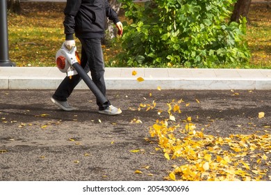 A Man, A Utility Worker, Removes Leaves From The Road With A Special Device.