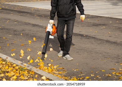 A Man, A Utility Worker, Removes Leaves From The Road With A Special Device.