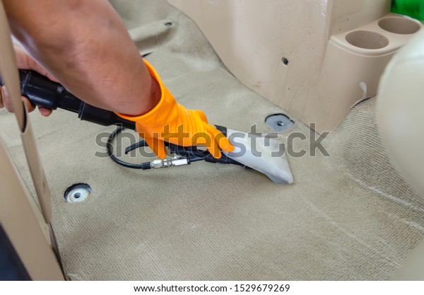 Man vacuuming the carpet cleaning equipment inside\
the car.