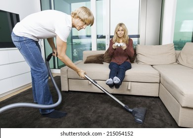 Man Vacuuming While Woman Play Video Game In Living Room At Home