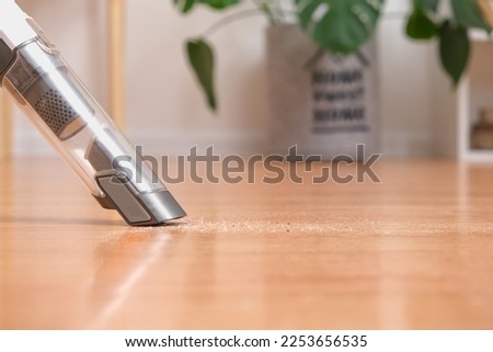 A man vacuums the floor with a portable vacuum cleaner. Cleaning the floor with a portable wireless handheld vacuum cleaner. Lightweight wireless, compact, portable cleaner.