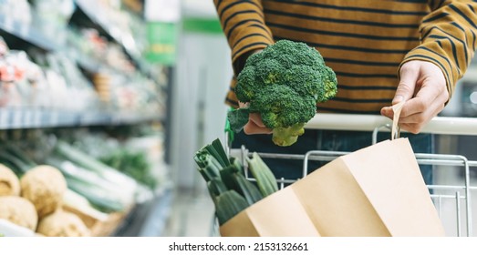 Man in the vegetable department at supermarket puts broccoli in the paper bag, banner