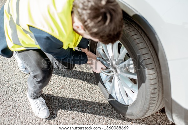 Man\
in vest unscrewing the broken wheel on the\
roadside