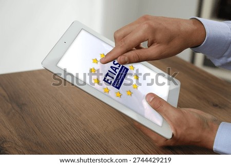 Man viewing ETIAS webpage using tablet computer at table, closeup. European Travel Information and Authorisation System