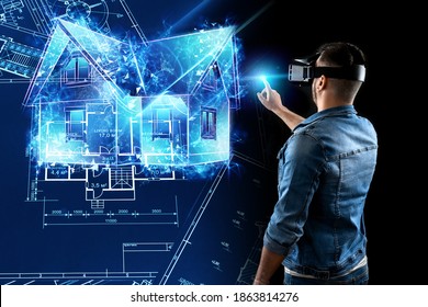 A Man In Virtual Reality Glasses Designs A Building A Hologram Of A House. Construction, Architecture Concept. Mixed Environment