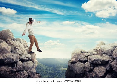 Man in virtual reality glasses is stepping carefully to walk on air between two high rocks on sunny valley - Powered by Shutterstock