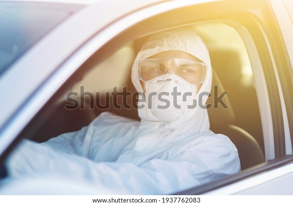 Man in virus protective suit and mask driving car. \
Man wearing protective hazmat rides in the car. The concept of\
preventing the spread of the epidemic, pandemic in quarantine city.\
Covid -19.