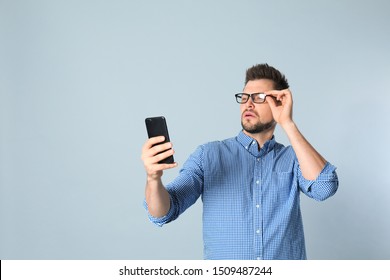 Man With Vision Problems Using Smartphone On Grey Background