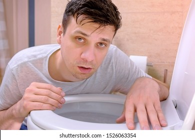 Man vomit in toilet sitting on floor looking at camera feeling bad having flu. Hangover, alcoholism, food poisoning and vomiting, cold and flu with high temperature. Sickness man at home with nausea.