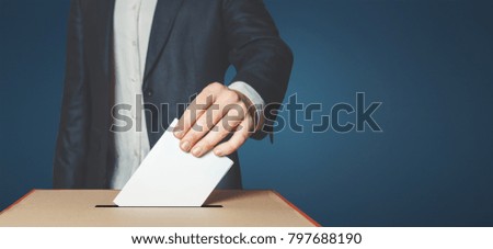 Man Voter Putting Ballot Into Voting box. Democracy Freedom Concept Near Blue Wall Copy-Space