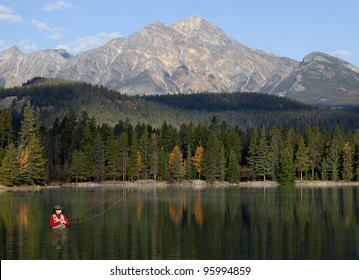 Man waist-deep in water fishing with reflections and mountains in background.