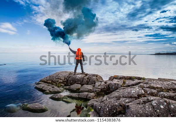 A man is waiting for help. The man stands on the\
chip with a torch in his hand. Smoke bomb. A signal for help. The\
man in the rescue jelly.