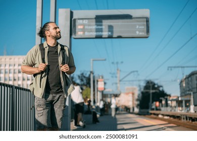 A man is waiting for a train on the platform. A young guy, a passenger with a backpack is standing on the platform waiting for the train - Powered by Shutterstock