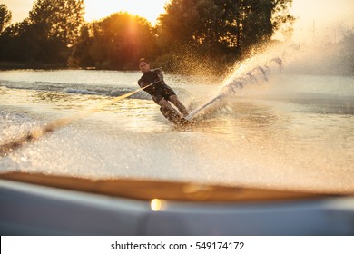 Man wakeboarding on lake behind boat. Water skiing on lake at sunset. - Powered by Shutterstock