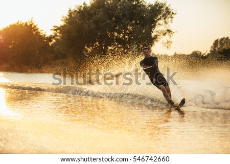 Man wakeboarding on a lake with splashes of water. Wakeboarder surfing across the lake.