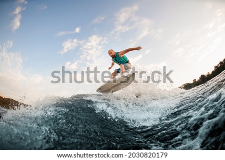Man wakesurfer jumping on wake board down the river waves. Surfer on wave. Male athlete training on wakesurf training.