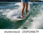 Man wakesurfing on a sunny day in a turquoise lake. Person surfing on a waterboard in blue water with sunlit waves