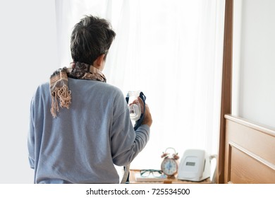  
Man Waking Up Freshly In The Morning Sitting And Holding Cpap Mask ,back View Backlighting And Cpap Machine In Background. Obstructive Sleep Apnea Therapy.