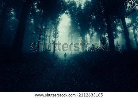 man walking alone on dark forest road at night