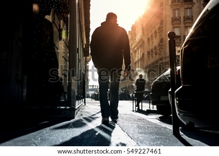 Man walking alone through the city road against sun