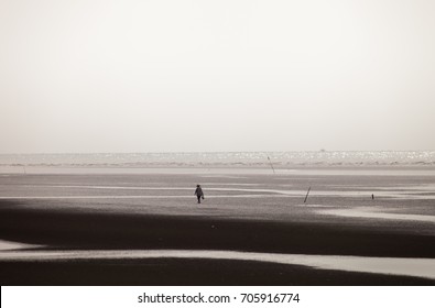 A man walking along black & white sand on the beach 