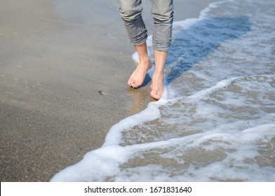 A man is walking along the golden sand of the beach. Male legs walking near the sea. Bare feet of a guy walking along a sandy shore with waves. Summer vacation or vacation.