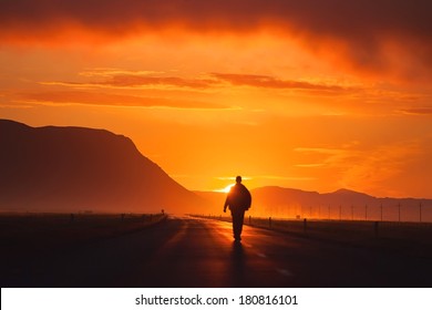 a man walking along the road, backlit at sunset, among the mountains, the clouds
