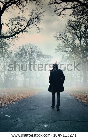 The man is walking along the road in the fog